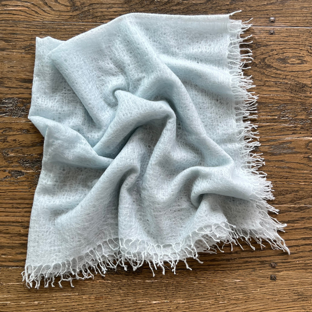 Light blue cashmere scarf with frayed edges on a wooden surface