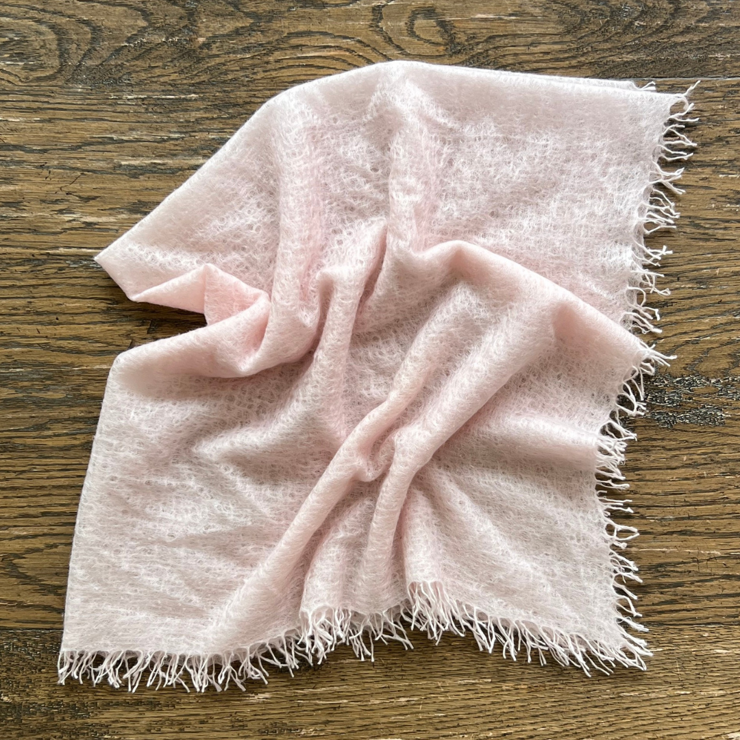 Baby Pink woven cashmere scarf with frayed edges on a wooden surface