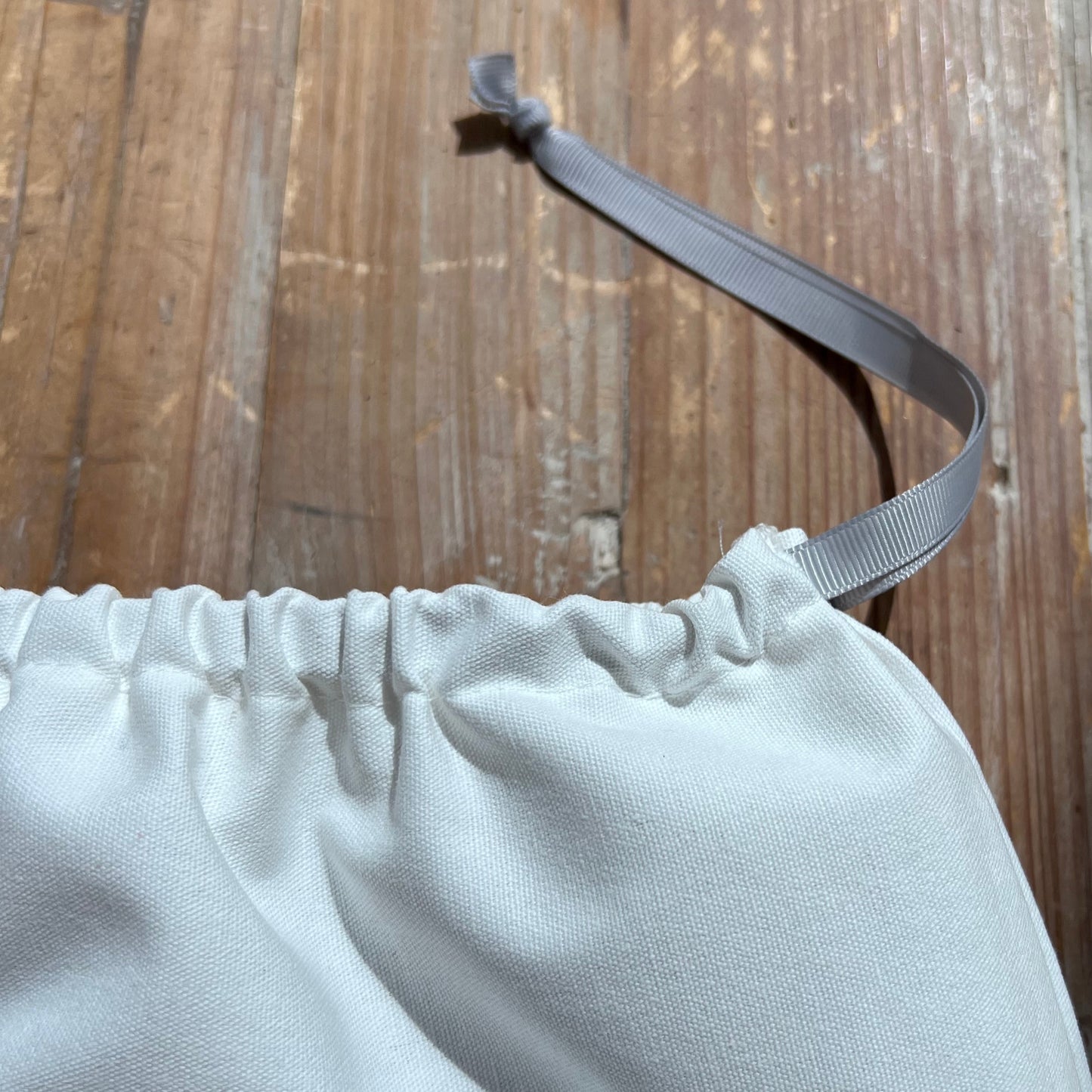 White canvas dust bag with a grey ribbon on a wooden surface