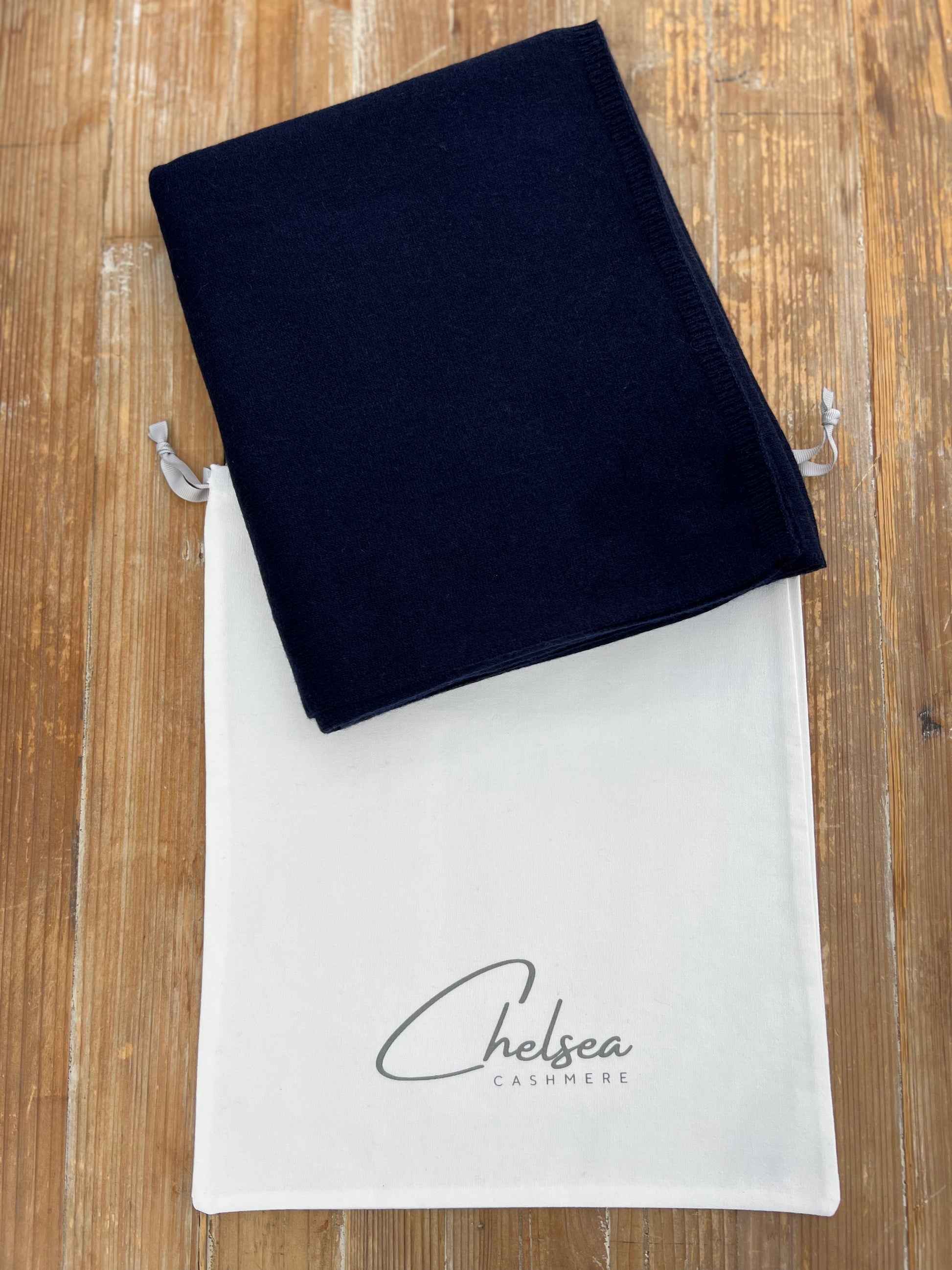 Navy cashmere scarf on a white drawstring bag with 'Chelsea Cashmere' branding