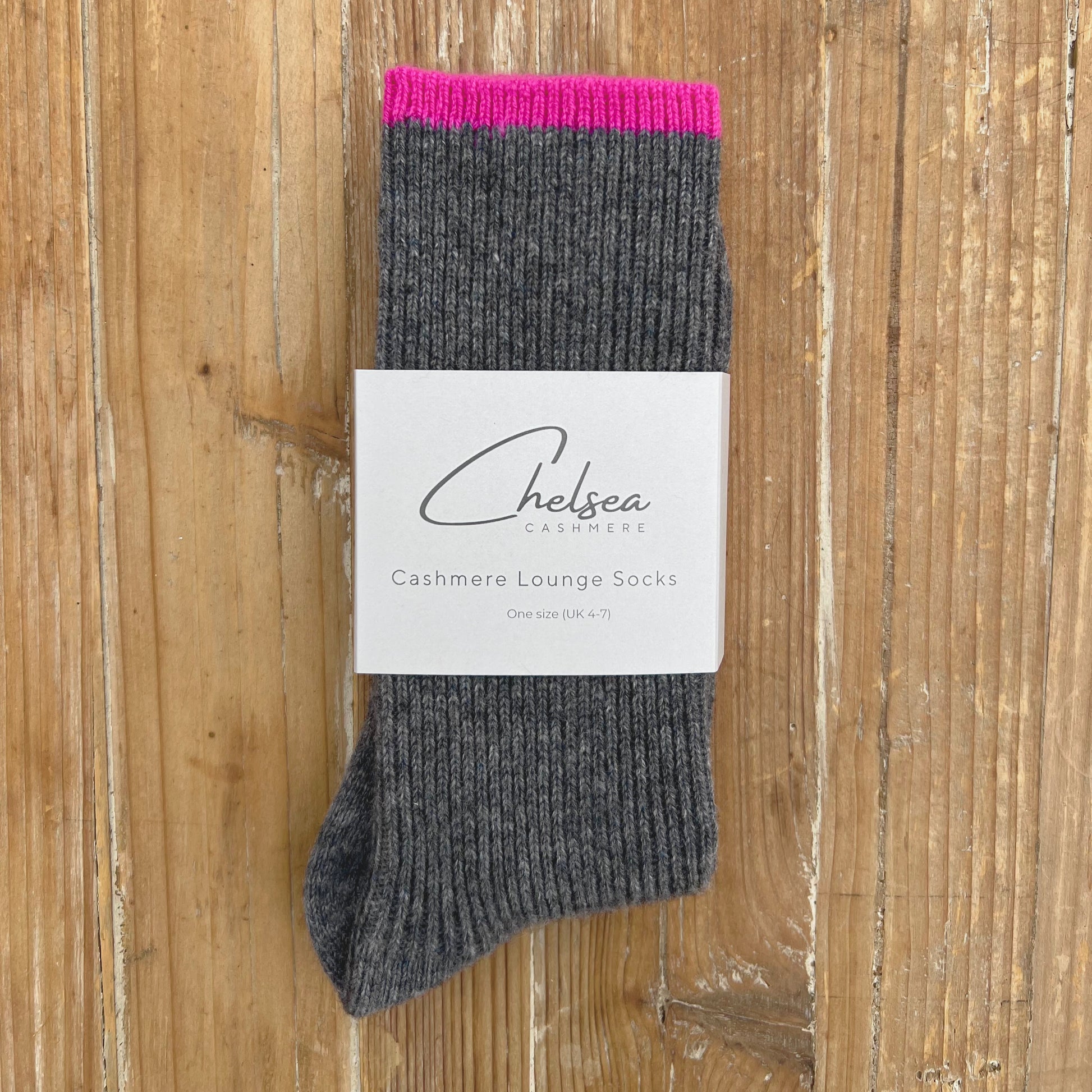 Gray cashmere lounge sock with pink cuff on a wooden surface, featuring the Chelsea Cashmere label.