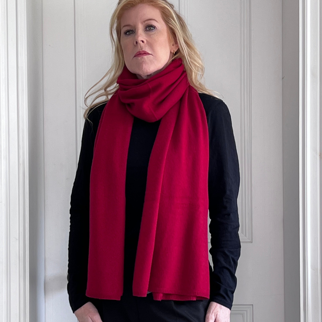Woman wearing a red cashmere scarf and black outfit against a white wall