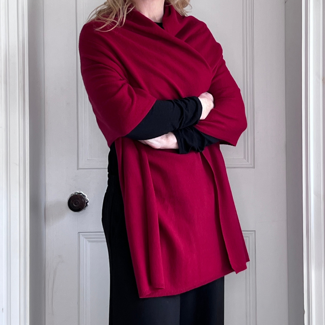 Woman wearing a red cashmere wrap and black outfit standing against a white wall.