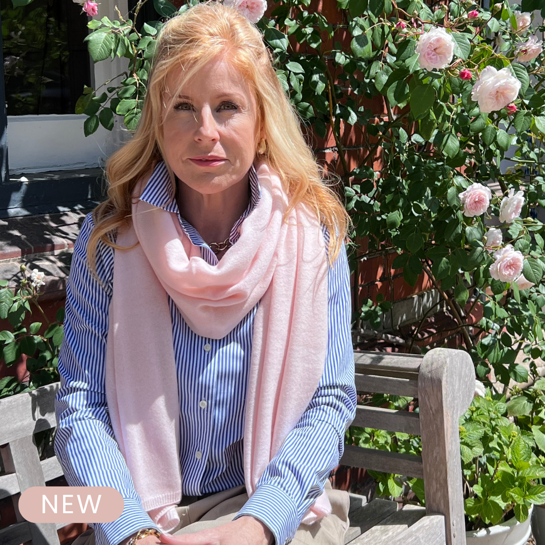 Woman wearing a pink cashmere scarf and blue striped shirt in a garden setting. Rose Cashmere Travel Wrap.