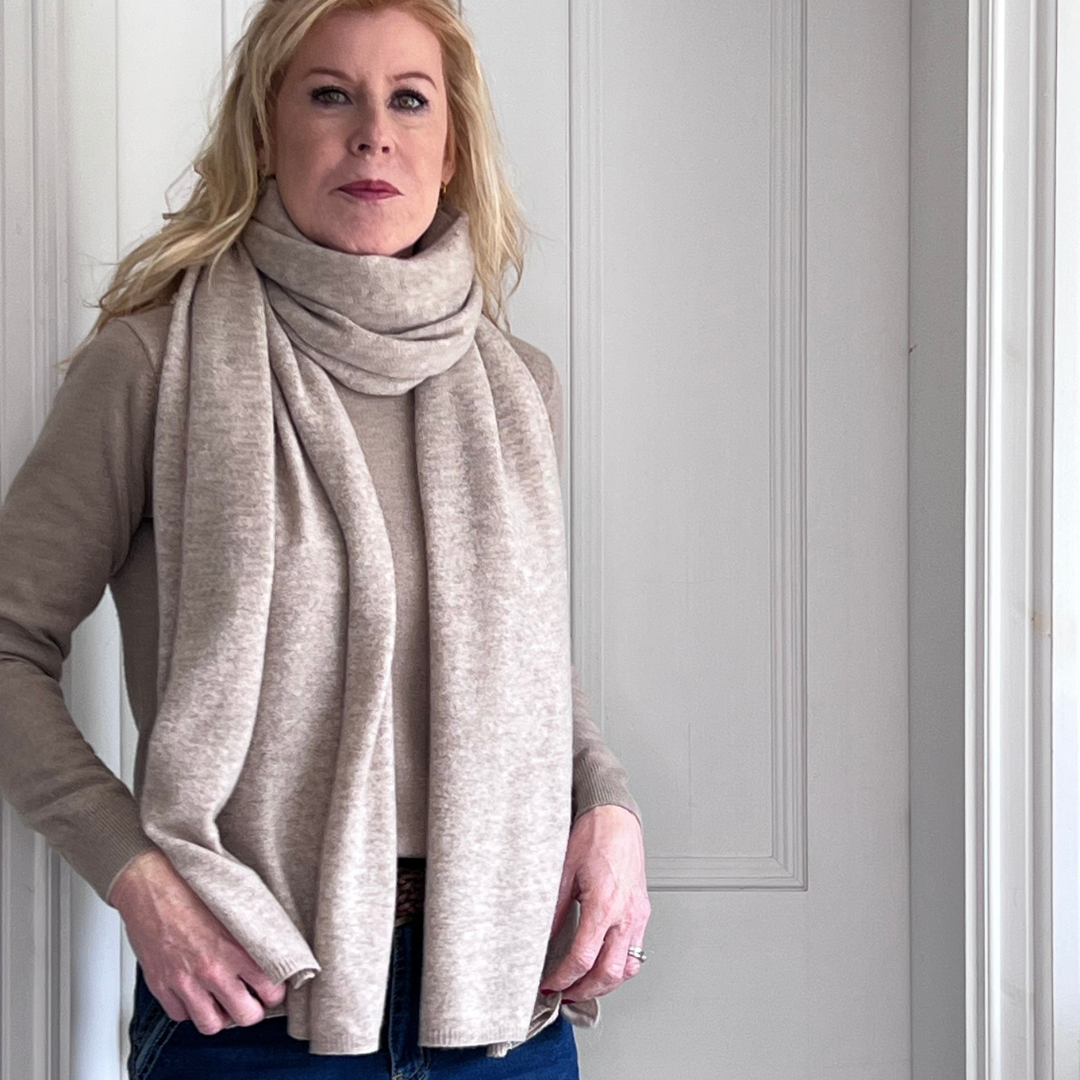 Woman wearing a sand beige cashmere scarf and blue jeans against a white wall