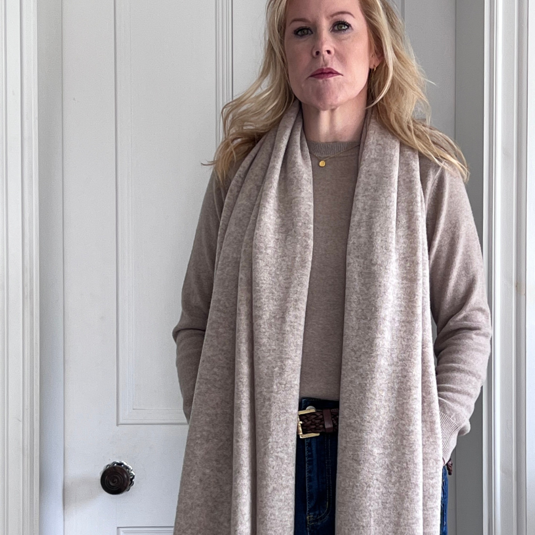 Woman wearing a sand cashmere scarf standing in front of a white door.