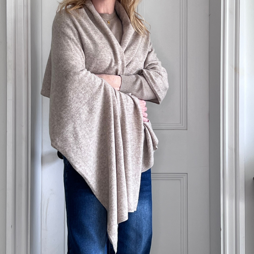 Woman wearing a sand beige cashmere wrap over her shoulders against a white wall.