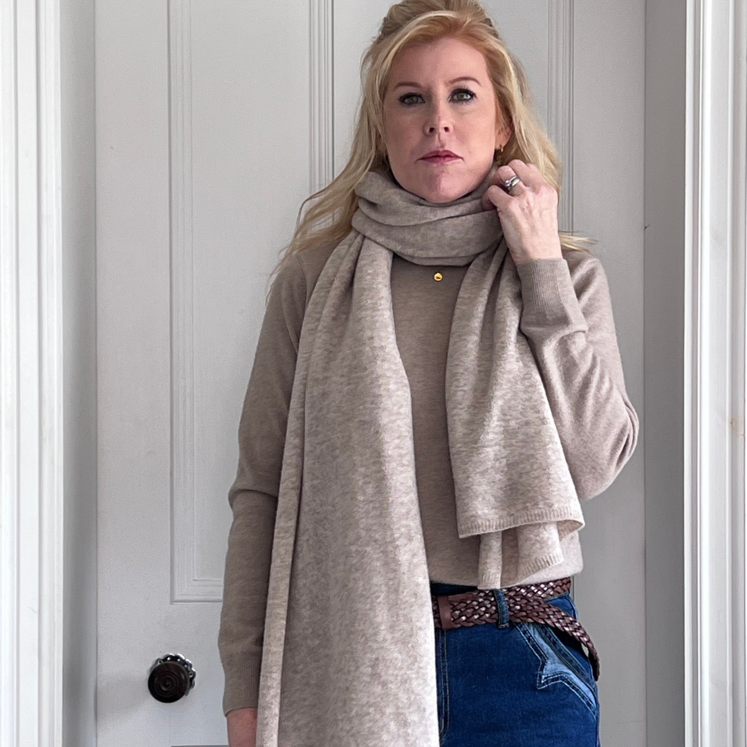 Woman wearing a sand cashmere scarf and brown sweater with jeans.