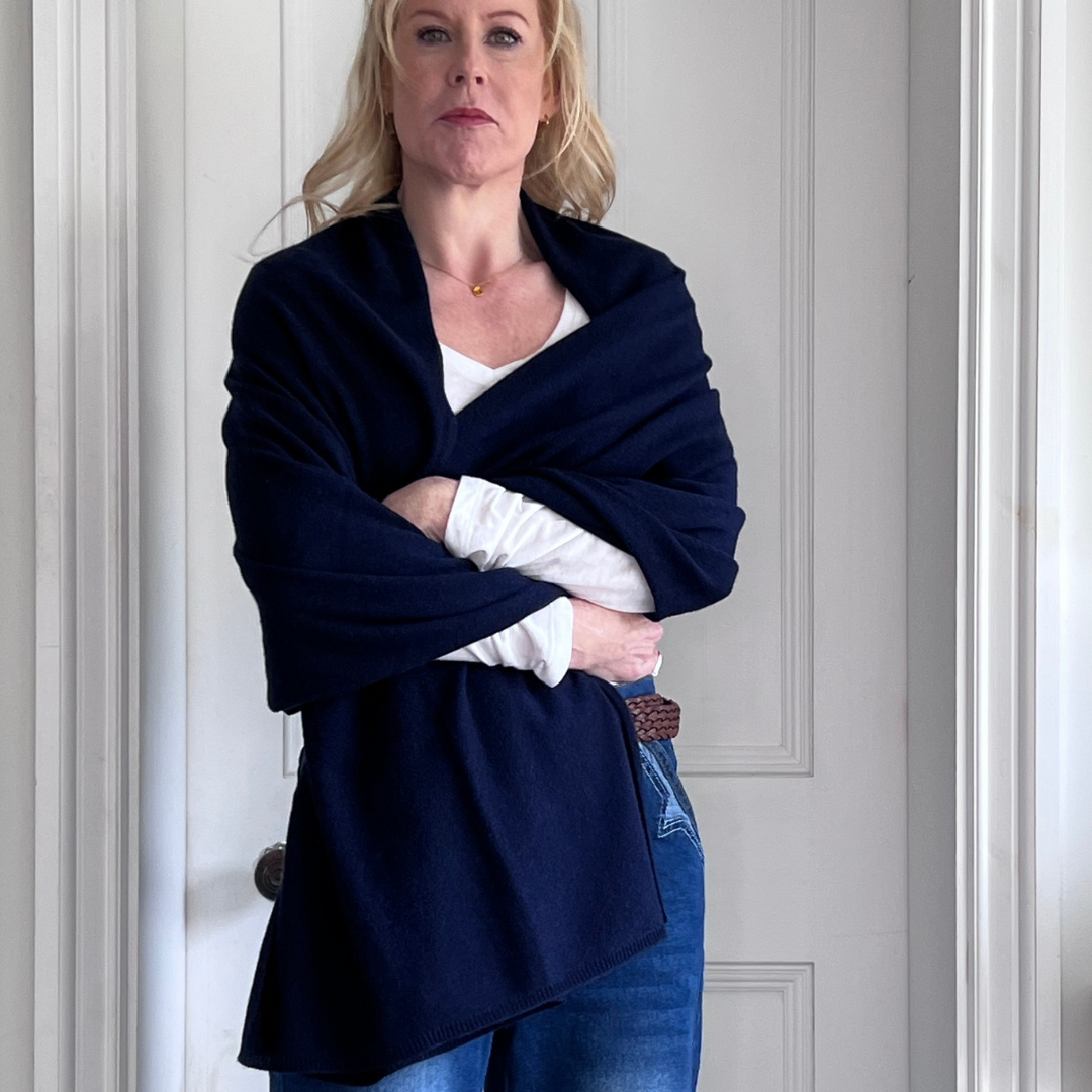 Woman wearing a navy blue cashmere shawl over a white top and blue jeans.