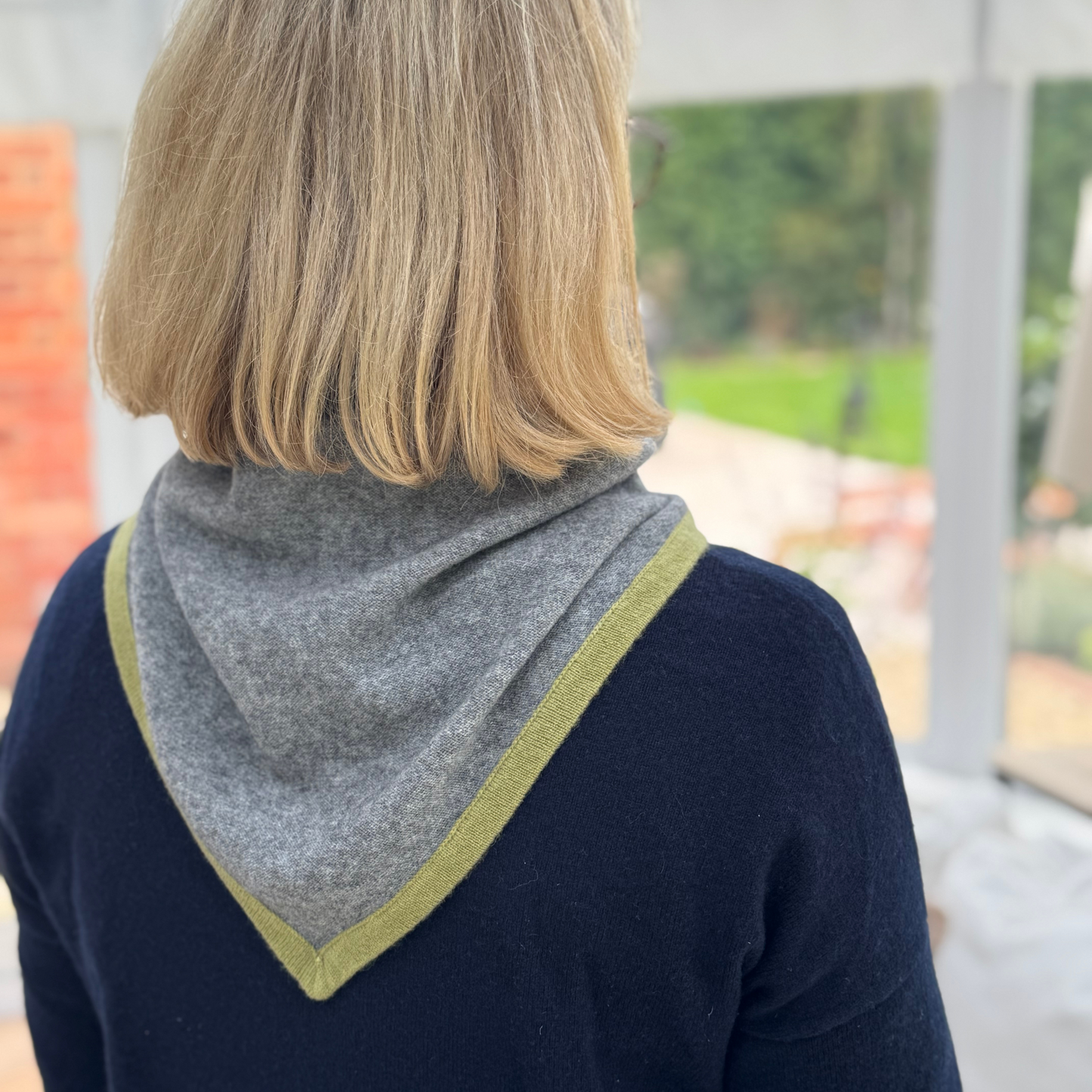 Person wearing a grey triangle cashmere scarf with green trim, over navy blue jumper