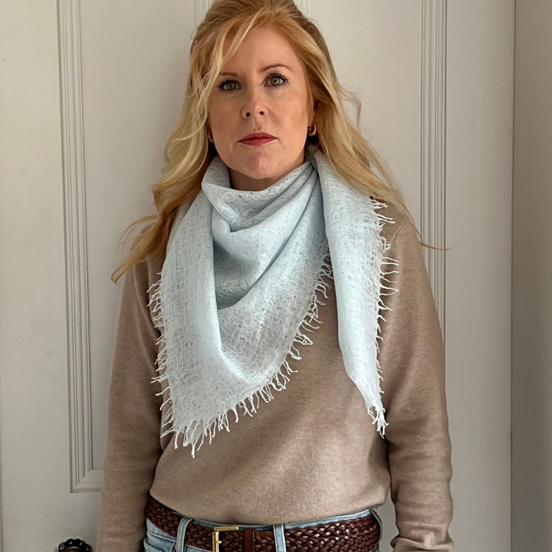 Woman wearing a light blue cashmere scarf and beige sweater against a neutral background