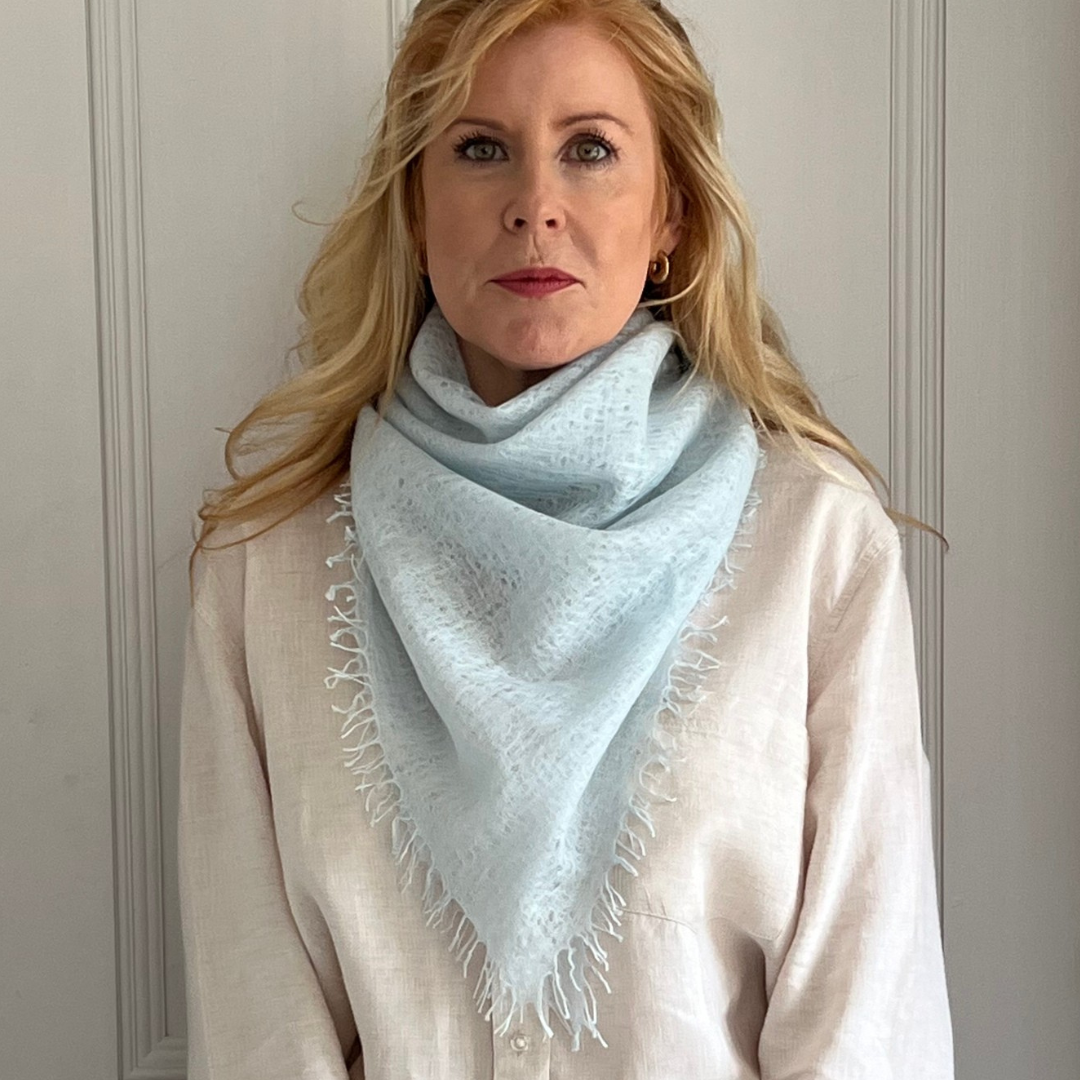 Woman wearing a light blue woven cashmere scarf against a neutral background