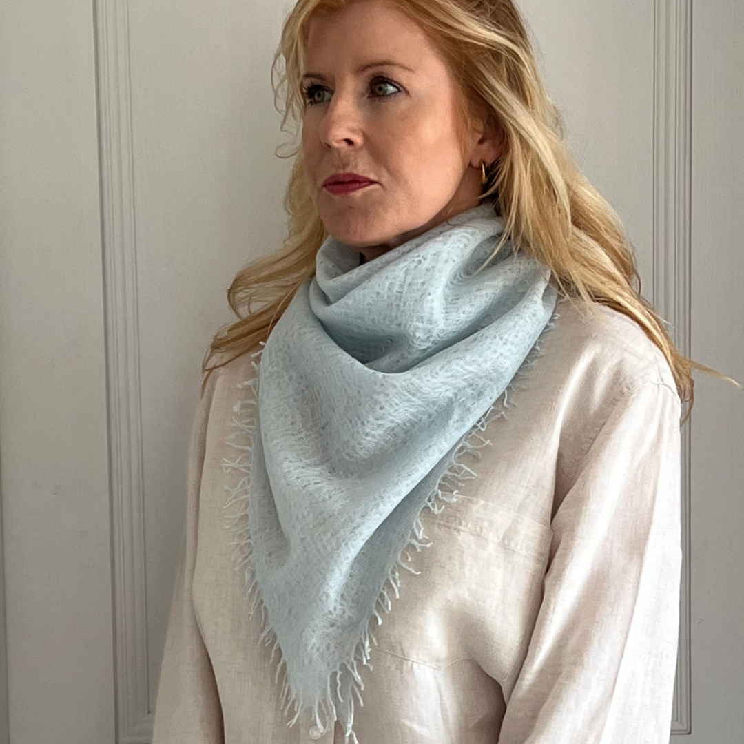 Woman wearing a light blue woven cashmere scarf with cream shirt
