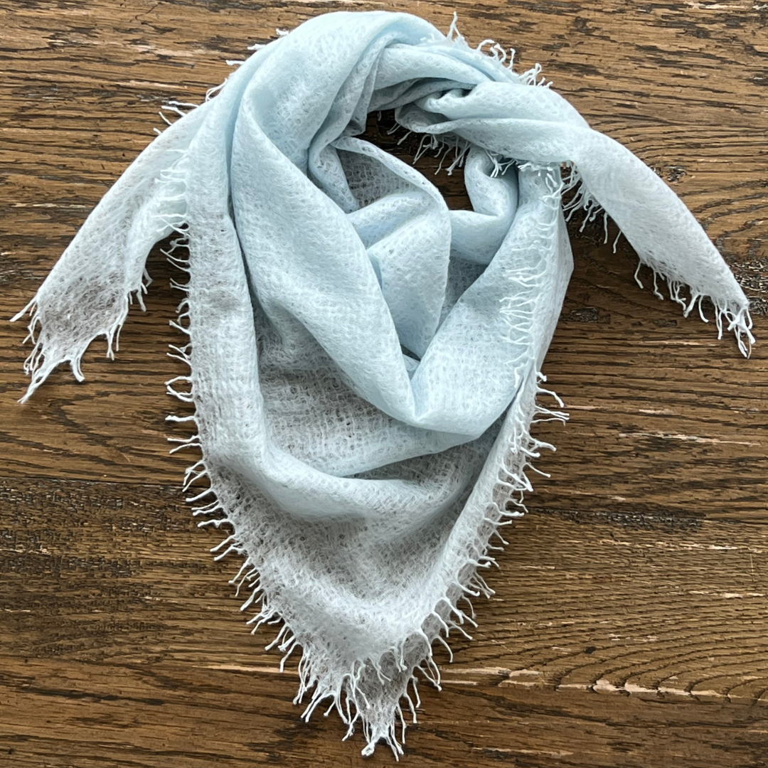 Light blue woven scarf with frayed edges on a wooden surface