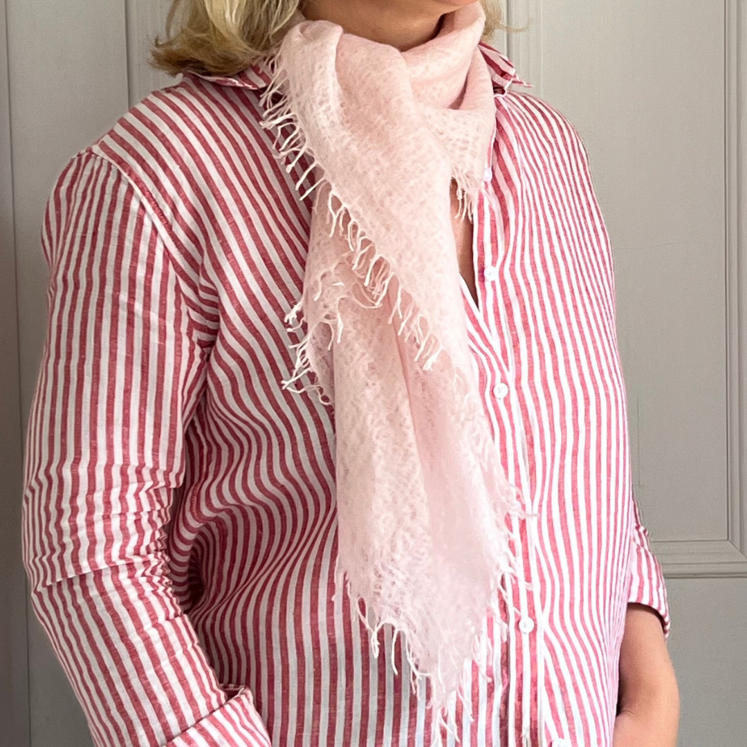 Person wearing a pink striped shirt and a light pink cashmere scarf with fringe details.
