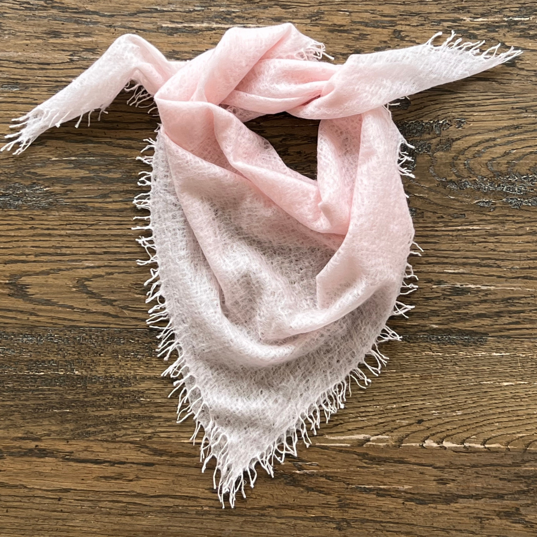 Light pink cashmere scarf with frayed edges on a wooden surface